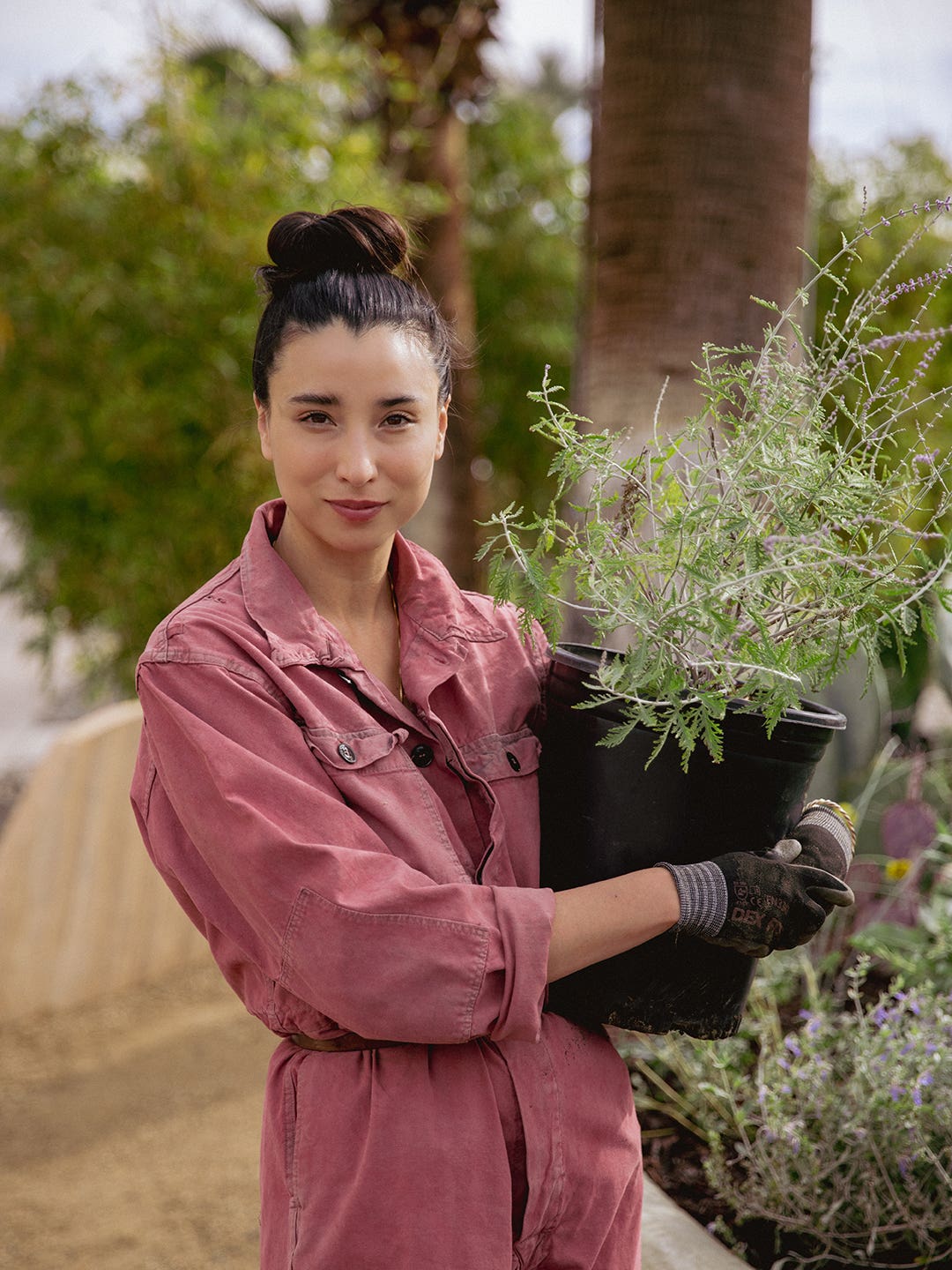 Lily Kwong in pink jumpsuit holding potted plant