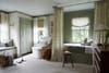 Nursery painted sage green with day bed, cream chair, and wood stool.