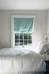 White room with bed and window with turquoise shade.