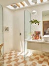 Bathroom with squiggly terracotta and white floor tile lit by a skylight. 
