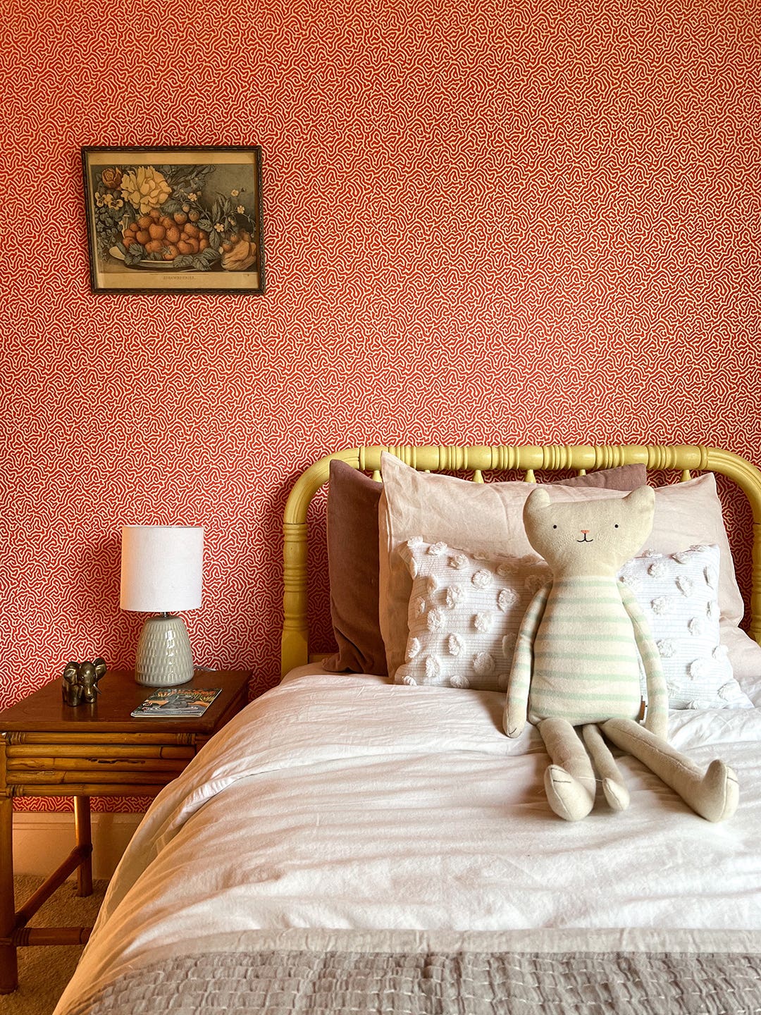 Kid's yellow bed with toy bunny and red wallpaper behind.