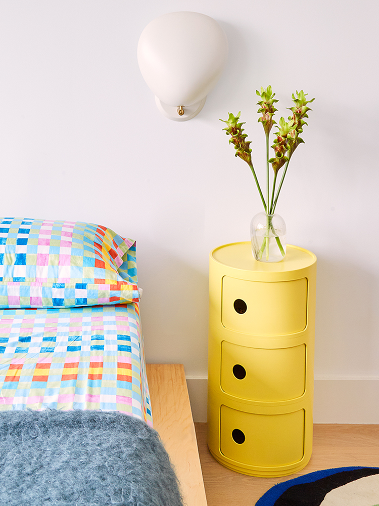 Yellow Kartell storage console next to colorful bed spread.