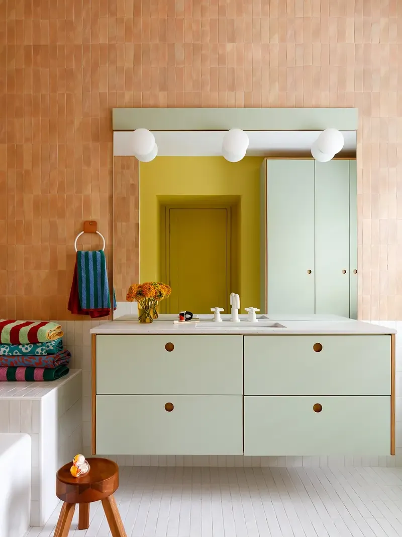 Bathroom with apricot-hued tiled wall and mint green floating vanity.