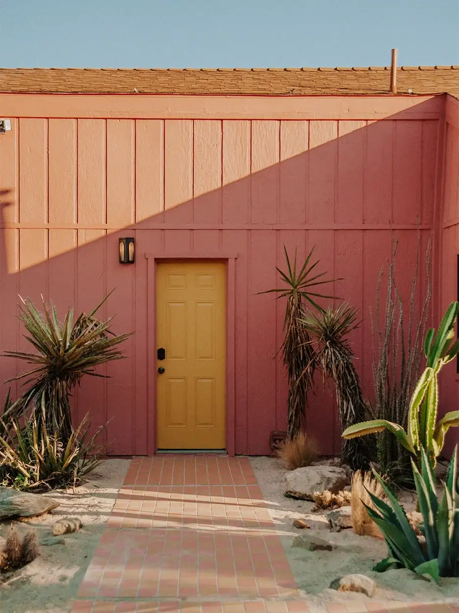 Pink house exterior with yellow door flanked by palm trees.