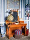 Teen bedroom with blue striped wallpaper and wood desk with striped blue and burgundy stool.